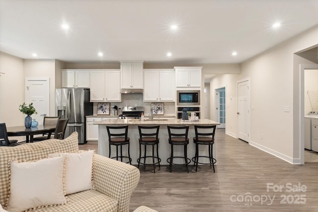 kitchen featuring light stone counters, stainless steel appliances, white cabinets, a kitchen island with sink, and a kitchen breakfast bar