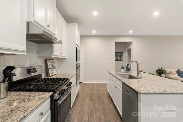 kitchen featuring a kitchen island with sink, under cabinet range hood, stainless steel appliances, a sink, and white cabinetry