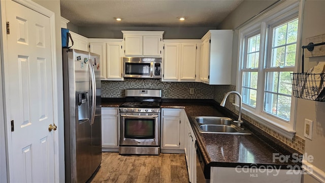 kitchen featuring stainless steel appliances, dark countertops, light wood-style flooring, decorative backsplash, and a sink