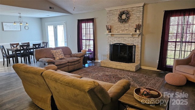 living room featuring a textured ceiling, wood finished floors, visible vents, vaulted ceiling, and a brick fireplace