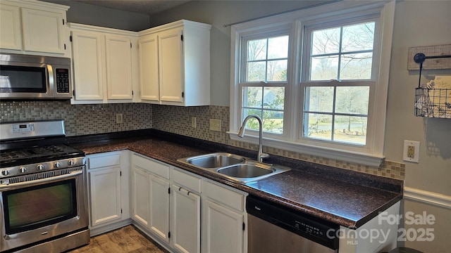 kitchen with tasteful backsplash, white cabinets, dark countertops, stainless steel appliances, and a sink