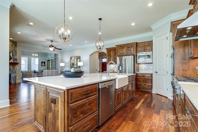 kitchen with an island with sink, hanging light fixtures, stainless steel appliances, and range hood