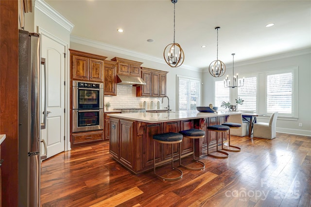 kitchen with a kitchen breakfast bar, stainless steel appliances, an island with sink, decorative light fixtures, and ornamental molding