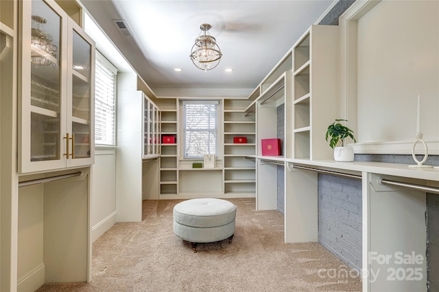 walk in closet with light colored carpet and an inviting chandelier