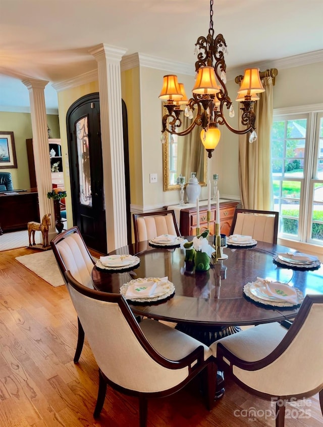 dining room with a chandelier, wood finished floors, decorative columns, and crown molding