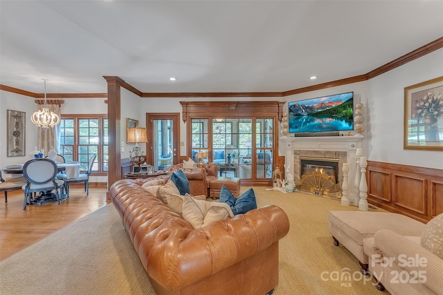 living area with crown molding, recessed lighting, an inviting chandelier, a high end fireplace, and wainscoting