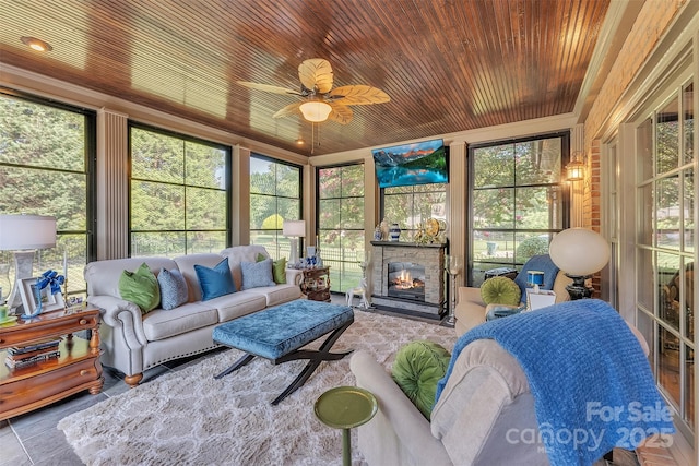 sunroom / solarium featuring plenty of natural light, ceiling fan, wooden ceiling, and a fireplace