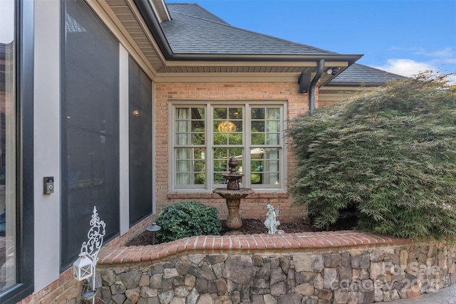 entrance to property featuring brick siding and roof with shingles