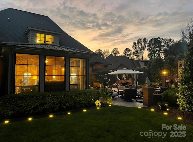 back of property at dusk featuring metal roof, a patio area, a yard, and a standing seam roof