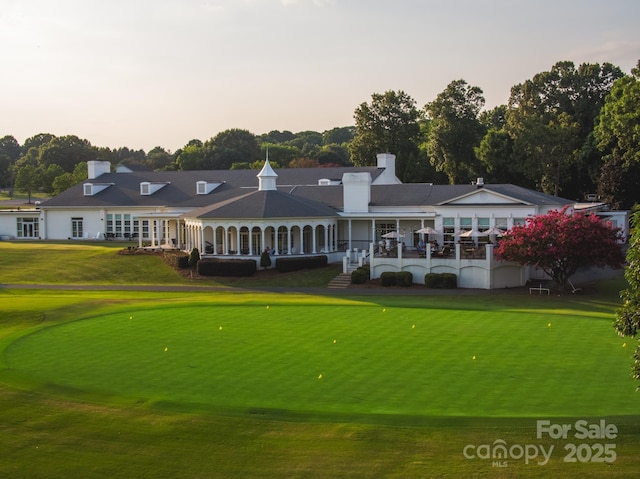 back of house at dusk featuring a chimney, golf course view, and a lawn