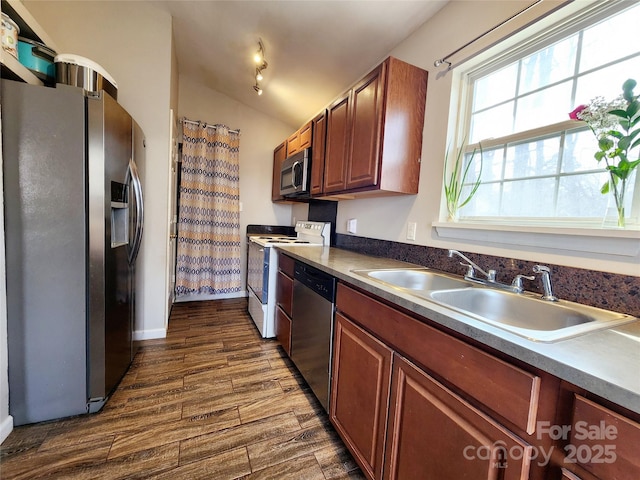 kitchen with dark countertops, dark wood-style flooring, vaulted ceiling, stainless steel appliances, and a sink