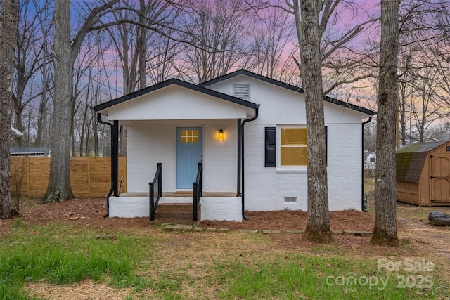 view of front of property with an outbuilding, a storage shed, brick siding, fence, and crawl space