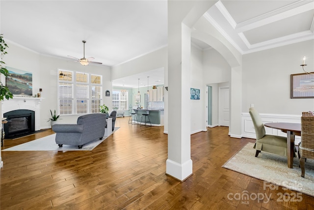 living room with arched walkways, ceiling fan, hardwood / wood-style flooring, a fireplace with flush hearth, and ornamental molding