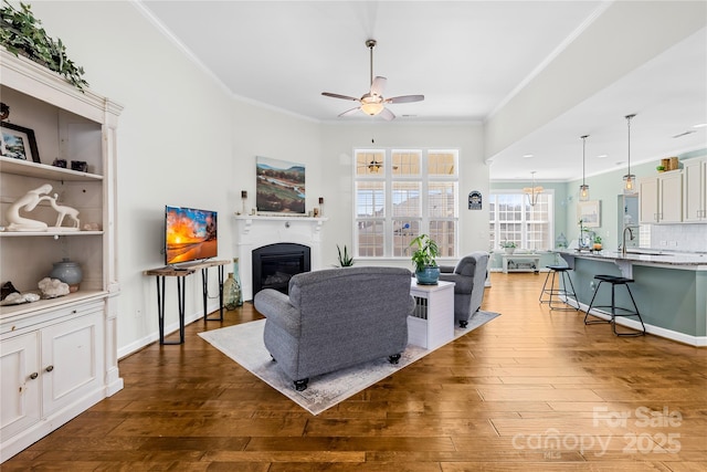 living area with hardwood / wood-style flooring, ornamental molding, a ceiling fan, and a glass covered fireplace