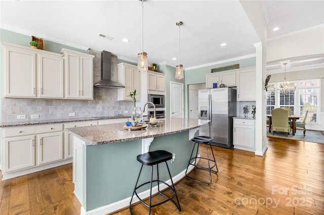 kitchen featuring stainless steel appliances, visible vents, wall chimney range hood, light wood-type flooring, and decorative backsplash