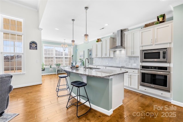 kitchen with crown molding, decorative backsplash, appliances with stainless steel finishes, a sink, and wall chimney exhaust hood