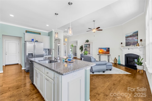 kitchen with light wood-style flooring, a fireplace with flush hearth, ornamental molding, open floor plan, and a sink