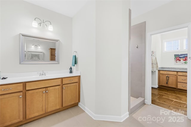 full bathroom featuring tiled shower, tile patterned flooring, vanity, and baseboards