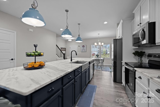 kitchen featuring sink, white cabinetry, decorative light fixtures, stainless steel appliances, and an island with sink