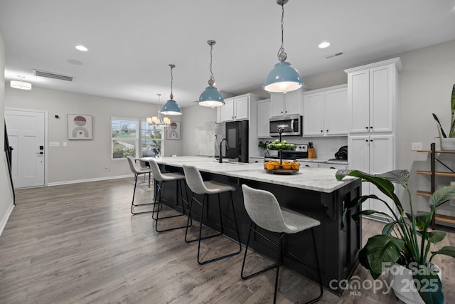 kitchen with white cabinetry, stainless steel appliances, decorative light fixtures, a large island with sink, and a breakfast bar area