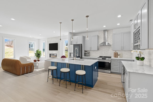 kitchen featuring appliances with stainless steel finishes, plenty of natural light, light wood-style flooring, wall chimney exhaust hood, and open floor plan