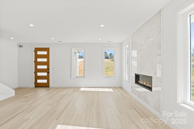 unfurnished living room with light wood-type flooring, plenty of natural light, and a fireplace