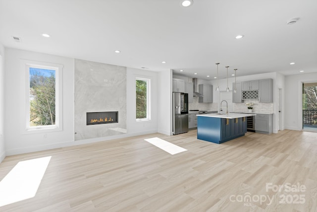 kitchen featuring a sink, stainless steel fridge with ice dispenser, gray cabinets, wall chimney range hood, and recessed lighting