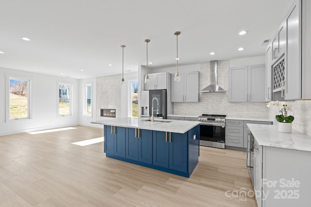 kitchen featuring wall chimney exhaust hood, stainless steel appliances, pendant lighting, light wood-style floors, and tasteful backsplash