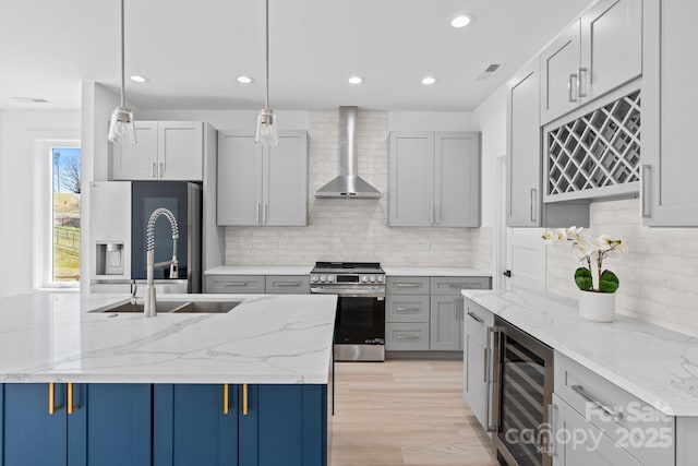 kitchen featuring a sink, stainless steel range with gas stovetop, wall chimney exhaust hood, fridge with ice dispenser, and wine cooler