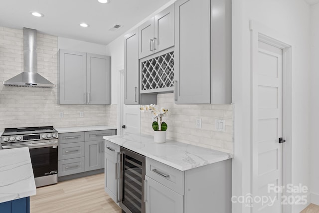 kitchen with light stone countertops, beverage cooler, wall chimney range hood, stainless steel range with electric stovetop, and gray cabinets