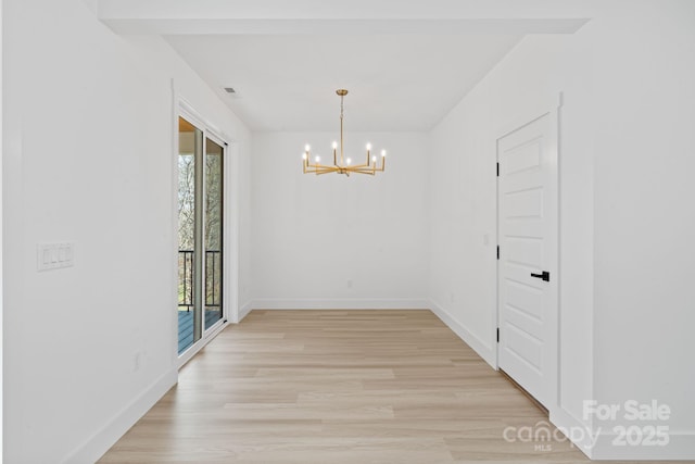 unfurnished dining area with baseboards, plenty of natural light, light wood-type flooring, and a chandelier