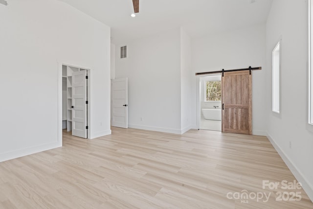 empty room with baseboards, a high ceiling, visible vents, and light wood-style flooring