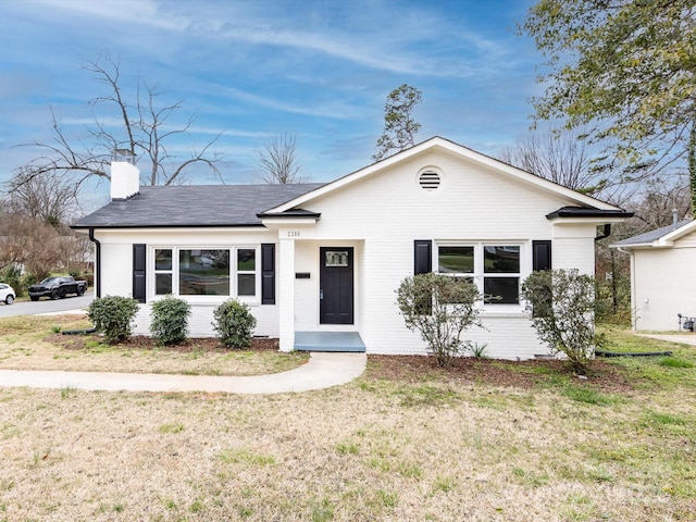 ranch-style home featuring a front yard, a chimney, and brick siding