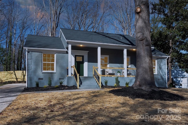 view of front facade with crawl space, a porch, brick siding, and fence