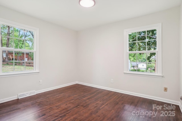 spare room with plenty of natural light, visible vents, baseboards, and dark wood finished floors