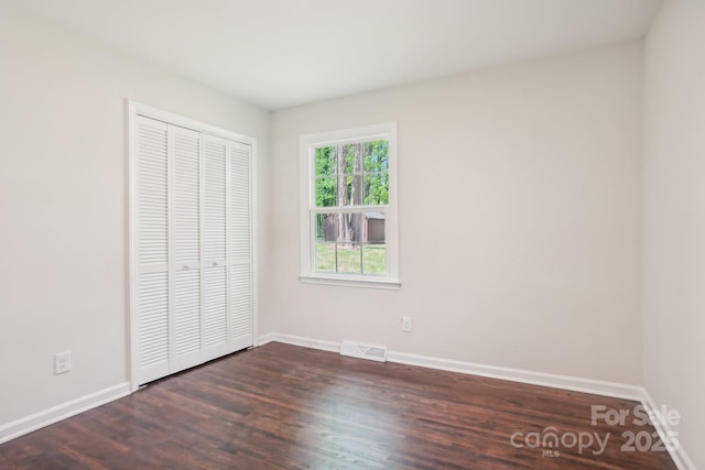 unfurnished bedroom with a closet, baseboards, dark wood finished floors, and visible vents