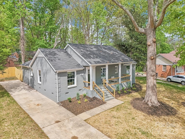 view of front of property featuring a porch, crawl space, concrete driveway, brick siding, and roof with shingles