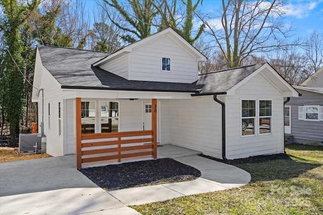 view of front of house with covered porch, central AC unit, a front lawn, and a shingled roof