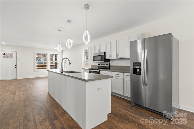 kitchen featuring dark wood-style flooring, dark countertops, hanging light fixtures, appliances with stainless steel finishes, and a sink