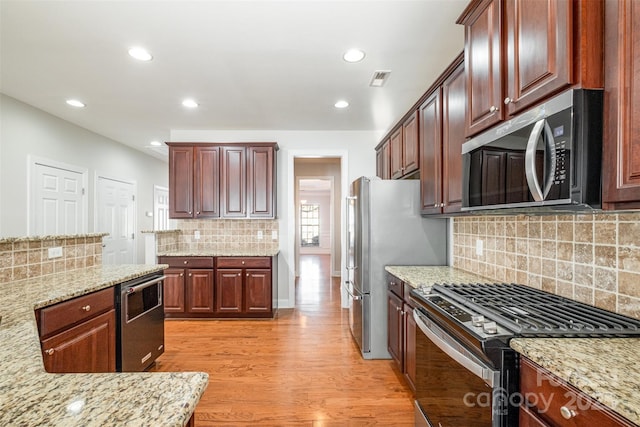 kitchen featuring light wood-type flooring, light stone countertops, stainless steel appliances, and decorative backsplash