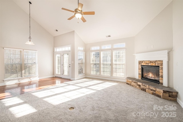 unfurnished living room featuring high vaulted ceiling, ceiling fan, a stone fireplace, and light colored carpet