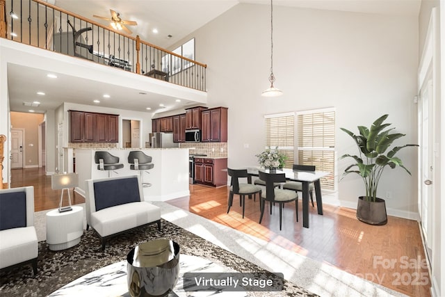 living room featuring a high ceiling, ceiling fan, and light hardwood / wood-style floors