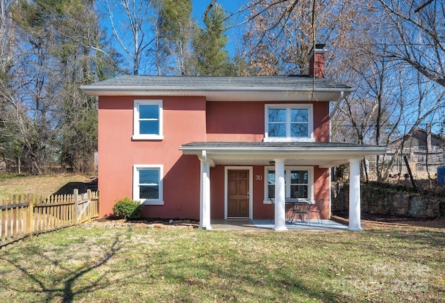 traditional-style house with a front lawn, a chimney, fence, and stucco siding