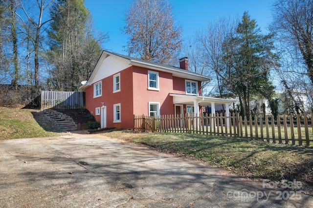 view of front of property featuring stairway, a fenced front yard, a chimney, and stucco siding