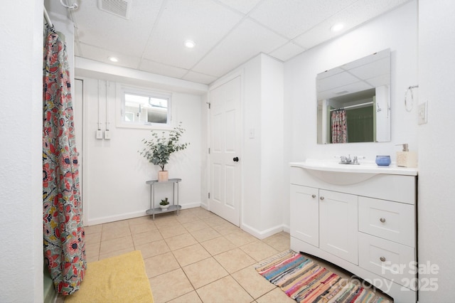 bathroom with a paneled ceiling, visible vents, vanity, tile patterned flooring, and baseboards