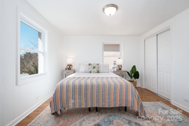 bedroom featuring a closet, multiple windows, baseboards, and wood finished floors