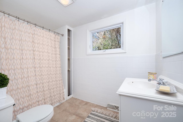 bathroom with toilet, wainscoting, tile walls, and vanity