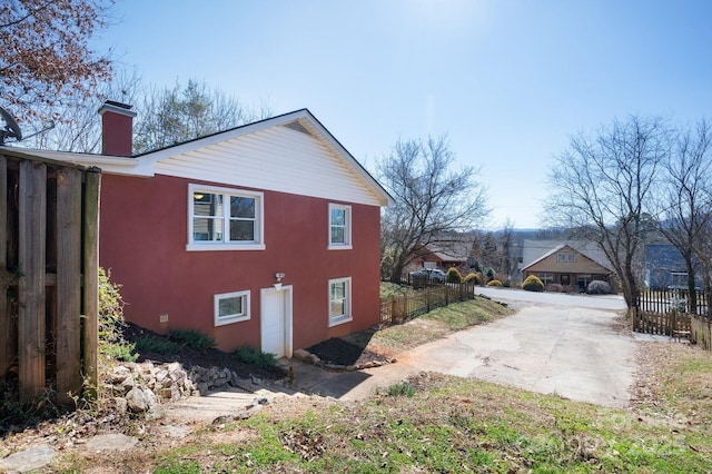 view of side of home with a chimney, fence, and stucco siding