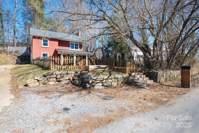 view of front facade with covered porch, a fenced front yard, a chimney, and stucco siding