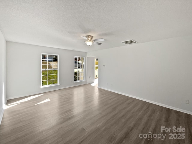 spare room featuring dark wood finished floors, visible vents, a ceiling fan, a textured ceiling, and baseboards